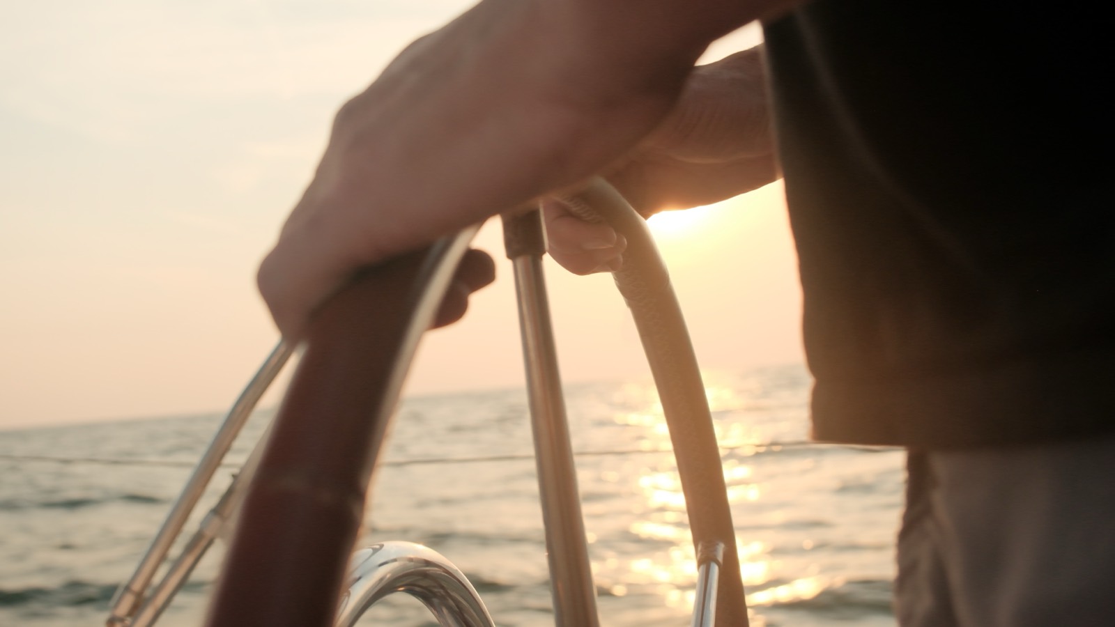 A sailor's hand on the helm of a yacht at sunset